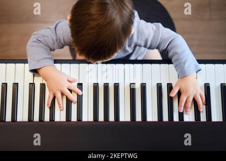 Le tout-petit joue du piano dans la salle de séjour, des cours de musique. Un enfant heureux apprend à jouer de la musique sur un piano électrique. Enfant garçon un an quatre mont Banque D'Images