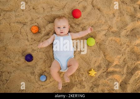 Vue de dessus d'un petit garçon heureux allongé sur une plage de sable Banque D'Images