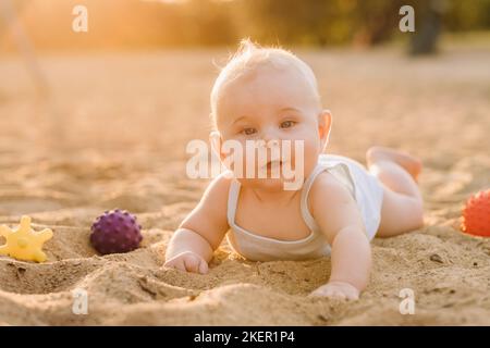 Un petit garçon heureux est couché sur une plage de sable près de la mer, aux rayons du soleil couchant Banque D'Images