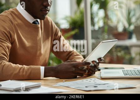 Homme d'affaires afro-américain utilisant une tablette numérique pour travailler en ligne tout en étant assis sur son lieu de travail au bureau Banque D'Images