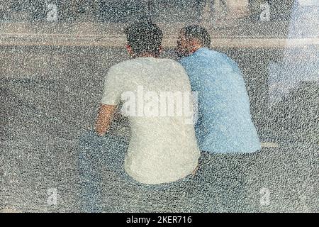 Deux personnes assises dans un abri de bus, vu à travers un mur de verre brisé. Bruxelles. Banque D'Images