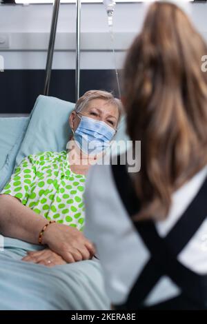 Petite fille méconnue qui parle à la grand-mère à l'hôpital. Vieille dame appréciant la compagnie de la petite-fille dans la salle de sanatorium. Une femme plus âgée se rétablissant de la maladie visitée par une jeune fille. Banque D'Images