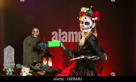 Jeune femme tenant un téléphone portable avec écran d'accueil en studio, montrant vide modèle d'espace de copie. Modèle habillé comme une déesse sainte avec une maquette de clé de chroma isolée sur smartphone. Banque D'Images