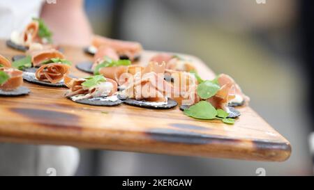 Plateau rustique en bois avec canapés ou amuse-gueule. Papillotes de cachets noirs avec du fromage et de la viande séchée comme le prosciutto roulé et petite feuille verte Banque D'Images