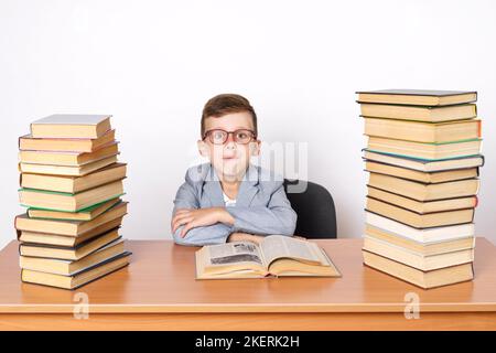 Concept d'éducation. Un étudiant avec des lunettes est assis à une table avec des livres des deux côtés. Banque D'Images