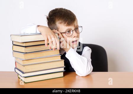 Concept d'éducation. L'étudiant s'assoit à la table et tient sa tête, les mains fonctionnent sur les livres empilés, regarde sur le côté. Isolé sur fond blanc Banque D'Images