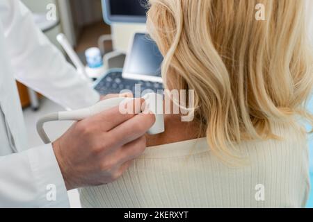vue rognée du médecin examinant le système lymphatique de la femme blonde avec l'échographie, image de stock Banque D'Images