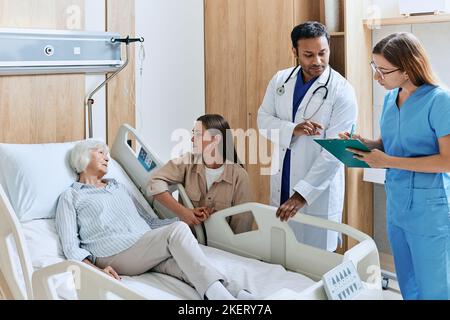 médecin avec infirmière faisant tour de la salle d'hôpital avec une femme âgée malade couchée sur le lit. Consultation au chevet du patient Banque D'Images