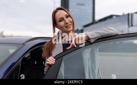 une femme d'affaires aux cheveux rouges se tient à une porte ouverte sur la toile de fond d'un centre d'affaires Banque D'Images