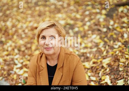 Chute de saison ou retraite: portrait en gros plan de la vieille femme caucasienne attrayante assise dans le parc d'automne. Des personnes âgées mûres et souriantes qui apprécient la nature. Photo de haute qualité Banque D'Images