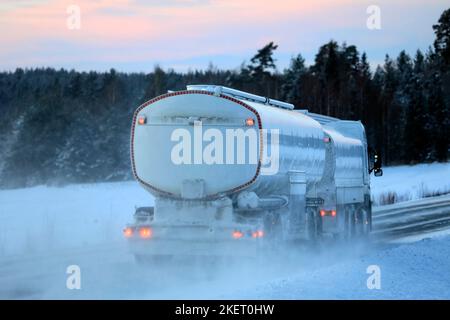 Vue arrière du camion-citerne à carburant enneigé le long de l'autoroute en hiver au coucher du soleil. Banque D'Images