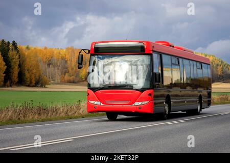 Bus avec front rouge sur l'autoroute à travers les paysages ruraux lors d'un jour couvert d'automne. Banque D'Images