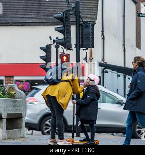 Epsom Surrey, Londres Royaume-Uni, 14 novembre 2022, mère et jeune fille sur Un Scooter debout à côté des feux de signalisation dans Un centre-ville de High Street Banque D'Images