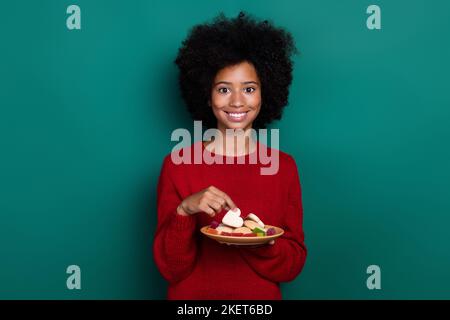 Photo de la petite fille adorable plaque de maintien biscuits sucrées bonbons maison porter vêtement tricoté rouge tendance isolé sur fond vert Banque D'Images