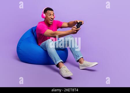 Photo de l'homme gai enjoué tendance tenue assis confort chaise look vide espace playstation relax repos isolé sur fond violet couleur Banque D'Images