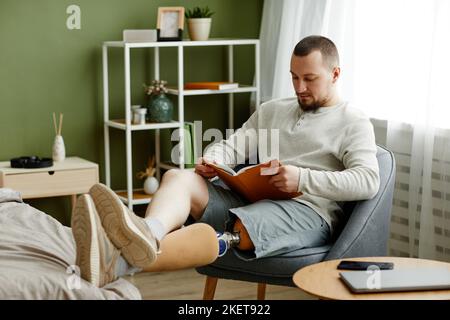 Portrait d'un homme adulte avec un livre de lecture prothétique de jambe à la maison et de détente, espace de copie Banque D'Images