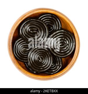 Roues de réglisse, dans un bol en bois. La réglisse, est une confestion, habituellement aromatisée et colorée en noir avec l'extrait des racines de la plante de réglisse. Banque D'Images