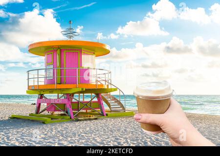 Main tenant une tasse de papier de café chaud et cabine au lever du soleil sur Miami Beach, Floride, États-Unis Banque D'Images