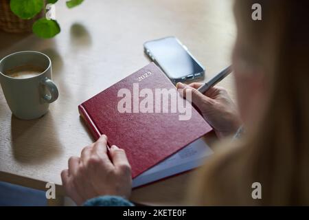 Gros plan de la femme mature écrivant dans le Journal du nouvel an 2023 à la maison Banque D'Images