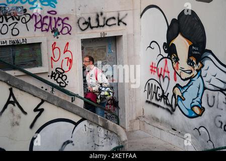 Un motocycliste en équipement de motard monte des marches avec des murs en béton couverts de graffiti dans le district de Santa Cruz, Lisbonne, Portugal, mars 2022. Banque D'Images