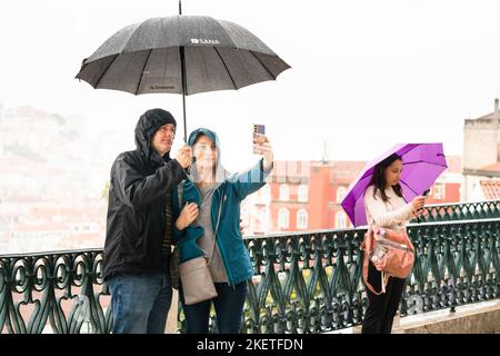 De fortes pluies se produisent et un couple prend un abri parapluie pour des photos et des selfies au Miradouro de São Pedro de Alcântara à Lisbonne, au Portugal. Banque D'Images