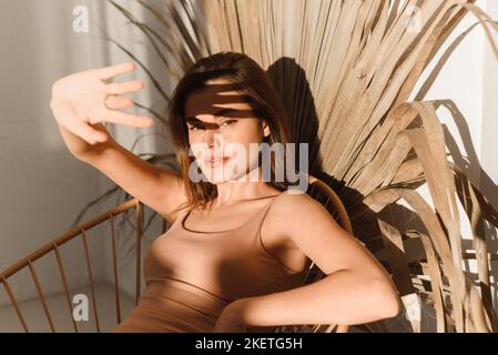 Jeune femme à la maison dans la salle de bains sur un fond d'ombres tropicales. Lumière du soleil, ombres des feuilles de palmier tropicales Banque D'Images