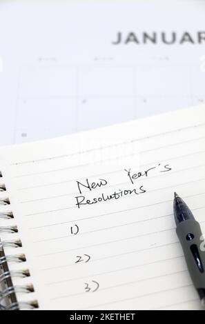 Bloc-notes avec la liste des résolutions du nouvel an et stylo à bille au premier plan en haut du calendrier de janvier en arrière-plan, sélection. Banque D'Images