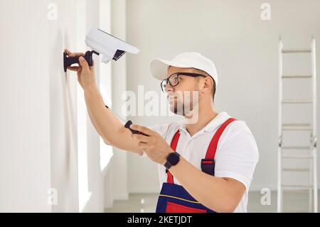 Un réparateur caucasien mâle en uniforme et lunettes tient un tournevis et installe la surveillance vidéo. Banque D'Images