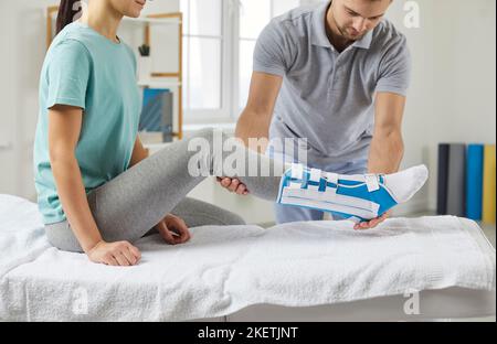 Un physiothérapeute masculin aide une femme à mettre une attelle de shin après une chirurgie de la jambe pendant la consultation médicale de réadaptation. Banque D'Images