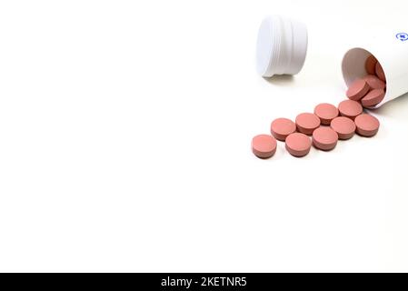 Des pilules de médecine rose débordent d'une bouteille blanche sur fond blanc Banque D'Images