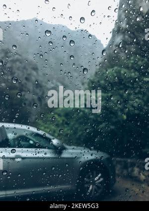 Gouttes de pluie sur l'image de verre de voiture propre avec voiture couleur argent sur l'arrière-plan. Automne profond froid pluie brouillard jour photo sur la place de stationnement de montagne. W Banque D'Images