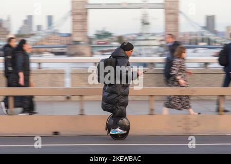 Un homme qui traverse un e-monocycle à travers le London Bridge, pendant l'heure de pointe. La conduite d'un e-monocycle privé est illégale en dehors de sur la propriété privée i Banque D'Images