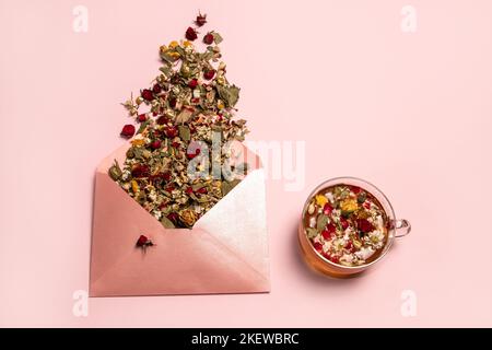 Fleurs sèches déversées d'une enveloppe rose brillante et d'une tasse de thé sur fond rose Banque D'Images