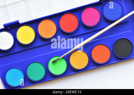 Peintures aquarelles colorées et pinceau fin dans une boîte bleue sur fond blanc gros plan, plan plat vue du dessus Banque D'Images
