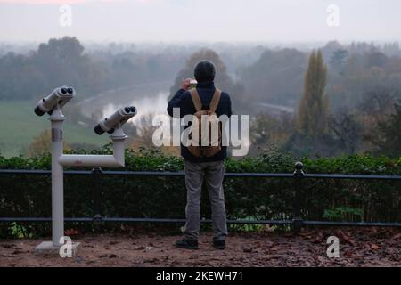 Londres, Royaume-Uni. 14th novembre 2022. Un homme prend une photo de la vue à l'avant. La brume s'attarde sur la Tamise au-dessus de Richmond avant le coucher du soleil après que la brume dense à Londres a entraîné l'annulation des vols ce matin. Crédit : onzième heure Photographie/Alamy Live News Banque D'Images