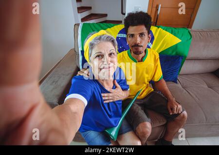 Mère et fils célébrant la coupe dans le salon en regardant la télévision acclamations pour le Brésil. Mixed Race Family prenant une photo de selfie tout en regardant un match de coupe. Banque D'Images