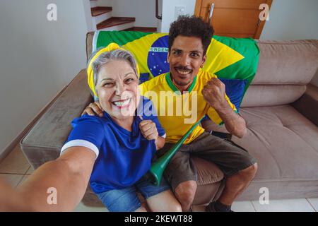 Mère et fils célébrant la coupe dans le salon en regardant la télévision acclamations pour le Brésil. Mixed Race Family prenant une photo de selfie tout en regardant un match de coupe. Banque D'Images