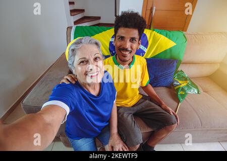 Mère et fils célébrant la coupe dans le salon en regardant la télévision acclamations pour le Brésil. Mixed Race Family prenant une photo de selfie tout en regardant un match de coupe. Banque D'Images