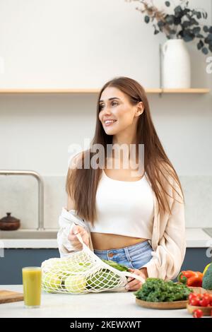 Une femme attirante prend des aliments frais dans un sac réutilisable en filet. Zéro déchet, une alimentation saine. Banque D'Images