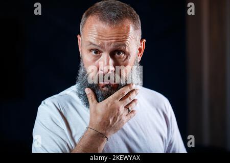 Portrait émotionnel d'un homme adulte aux cheveux gris avec une barbe dans un t-shirt blanc Banque D'Images