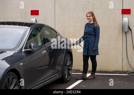 Bonne jolie jeune femme souriante charge la voiture électrique moderne Banque D'Images