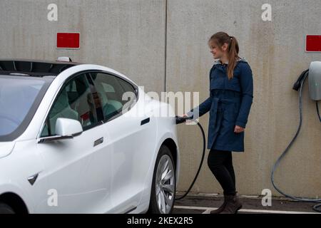 Bonne jolie jeune femme souriante charge la voiture électrique moderne Banque D'Images