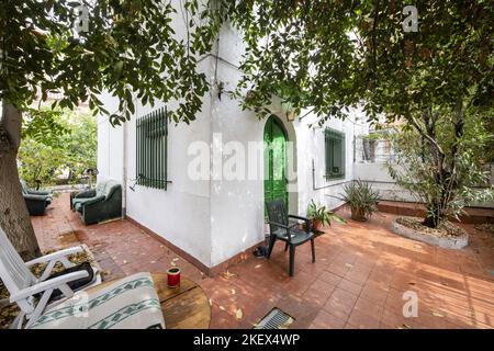 Espace de loisirs et de repos avec tables, bancs et arbres dans une maison familiale avec un sol en grès brun et une façade blanche Banque D'Images