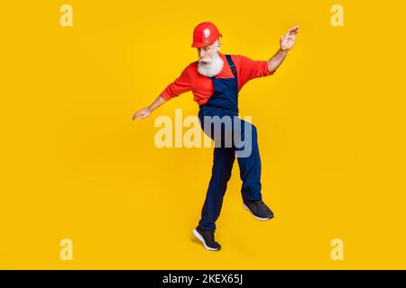 Photo de l'âge funky positif homme vêtements de travail général Red Hat dur danse ayant amusant isolé couleur jaune fond Banque D'Images