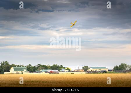 Un plumeau de récolte volant au-dessus d'une ferme rustique après avoir pulvérisé une récolte dans les Prairies canadiennes dans le comté de Rocky View Alberta Canada. Banque D'Images