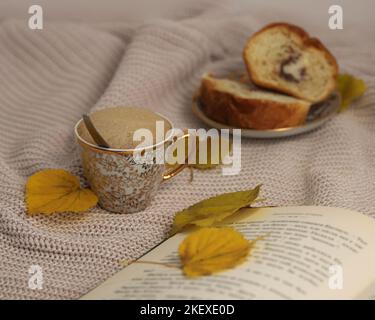 Une tasse de café sur la table, un livre ouvert, un dessert, un pull chaud et des feuilles d'automne jaunes en gros plan, le concept d'un matin d'automne confortable Banque D'Images