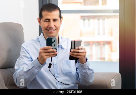 Happy man charge un smartphone avec un chargeur portable installé sur un canapé à la maison Banque D'Images