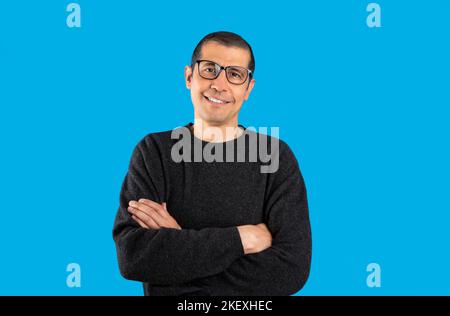 Photo en studio d'un homme portant un chandail décontracté et des lunettes sur fond bleu visage heureux souriant avec des bras croisés regardant l'appareil photo. Pers. Positives Banque D'Images