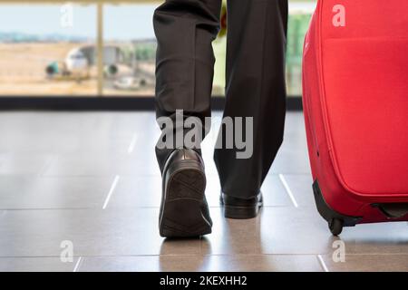 Vue arrière des jambes de l'homme en voyage marchant avec une valise dans un aéroport Banque D'Images