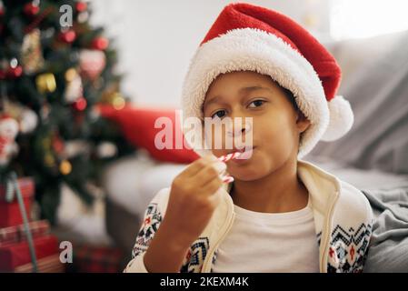 Gros plan sur un garçon afro-américain portant un chapeau de père Noël qui se réglisse de canne à sucre célébrant le Noël du nouvel an Banque D'Images